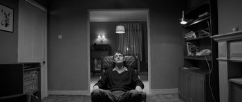 Movie still from “Control” (2007), directed by Anton Corbijn – A man sitting in a chair in front of a doorway; Medium shot, Low angle