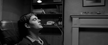 Movie still from “Control” (2007), directed by Anton Corbijn – A young man sitting in front of a book shelf; Close Up shot, Low angle