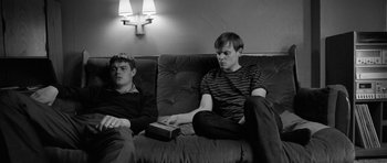Movie still from “Control” (2007), directed by Anton Corbijn – Two young men sitting on a couch watching television; Medium shot, High angle