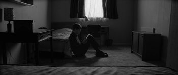 Movie still from “Control” (2007), directed by Anton Corbijn – A man sitting on the ground reading a book; Wide shot, High angle