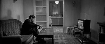 Movie still from “Control” (2007), directed by Anton Corbijn – A man sitting at a table in a room; Wide shot, High angle