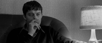 Movie still from “Control” (2007), directed by Anton Corbijn – A man sitting in a chair with a cigarette in his mouth; Close Up shot, Over the shoulder angle