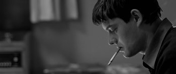 Movie still from “Control” (2007), directed by Anton Corbijn – A young man is smoking a cigarette in a room; Close Up shot, Low angle