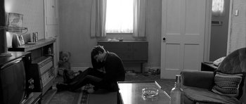 Movie still from “Control” (2007), directed by Anton Corbijn – A man sitting on the floor of a living room; Medium shot, High angle