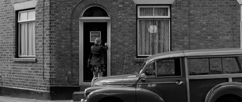 Movie still from “Control” (2007), directed by Anton Corbijn – An older woman standing in front of an open door; Wide shot, Over the shoulder angle