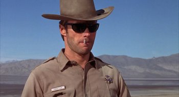 Movie still from “Coogan's Bluff” (1968), directed by Don Siegel – A man in a hat and sunglasses is smoking a cigarette; Medium shot, Low angle