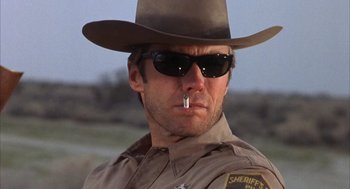 Movie still from “Coogan's Bluff” (1968), directed by Don Siegel – A man in a hat and sunglasses smoking a cigarette in his mouth; Close Up shot, Low angle