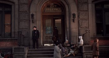 Movie still from “Coogan's Bluff” (1968), directed by Don Siegel – People sitting on the steps of a building with a police officer standing on the steps; Wide shot, High angle