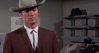 Movie still from “Coogan's Bluff” (1968), directed by Don Siegel – A man wearing a suit and a cowboy hat in a room; Medium shot, Low angle