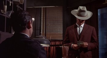 Movie still from “Coogan's Bluff” (1968), directed by Don Siegel – A man wearing a cowboy hat and a suit and tie; Medium shot, Over the shoulder angle