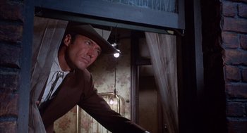 Movie still from “Coogan's Bluff” (1968), directed by Don Siegel – A man wearing a cowboy hat looking out a window; Medium shot, Low angle