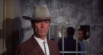 Movie still from “Coogan's Bluff” (1968), directed by Don Siegel – A man wearing a cowboy hat in front of a fence; Close Up shot, Low angle