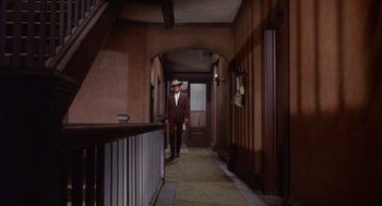 Movie still from “Coogan's Bluff” (1968), directed by Don Siegel – A man in a suit and hat walking down a hall way; Wide shot, High angle