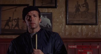 Movie still from “Coogan's Bluff” (1968), directed by Don Siegel – A man in a black jacket holding a stick in a room; Close Up shot, Low angle