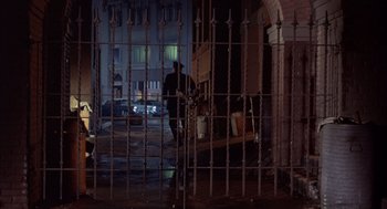 Movie still from “Coogan's Bluff” (1968), directed by Don Siegel – A man standing in front of an iron fence; Wide shot, High angle