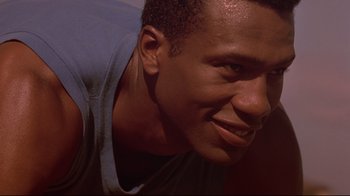 Movie still from “Cool Runnings” (1993), directed by Jon Turteltaub – A man smiling for the camera; Close Up shot, Low angle