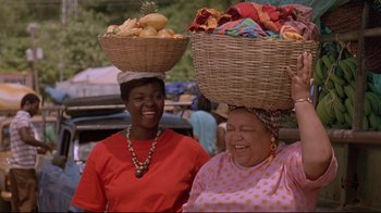 Movie still from “Cool Runnings” (1993), directed by Jon Turteltaub – Two women with baskets on their heads smile for the camera; Medium shot, Low angle