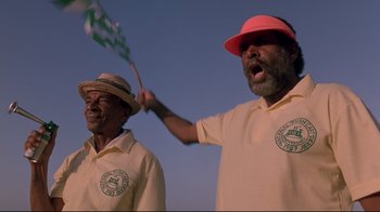 Movie still from “Cool Runnings” (1993), directed by Jon Turteltaub – Two men in yellow shirts and hats are holding a flag; Close Up shot, Low angle