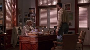 Movie still from “Cool Runnings” (1993), directed by Jon Turteltaub – Two men are sitting at a desk in a room; Wide shot, Over the shoulder angle