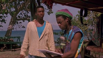 Movie still from “Cool Runnings” (1993), directed by Jon Turteltaub – A man standing next to another man writing on a piece of paper; Medium shot, Low angle