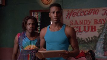 Movie still from “Cool Runnings” (1993), directed by Jon Turteltaub – Two young men standing in a room holding a book; Medium shot, Low angle