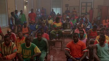 Movie still from “Cool Runnings” (1993), directed by Jon Turteltaub – A large group of people sitting in a room; Wide shot, High angle