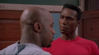 Movie still from “Cool Runnings” (1993), directed by Jon Turteltaub – Two men standing next to each other in front of a wall; Close Up shot, Over the shoulder angle