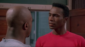Movie still from “Cool Runnings” (1993), directed by Jon Turteltaub – A man in a red t - shirt is talking to another man in a red shirt; Close Up shot, Over the shoulder angle