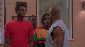 Movie still from “Cool Runnings” (1993), directed by Jon Turteltaub – A group of men standing next to each other in a room; Medium shot, Over the shoulder angle