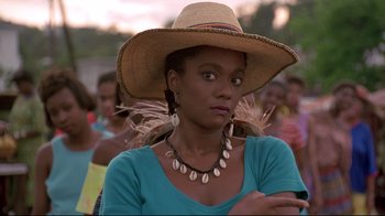 Movie still from “Cool Runnings” (1993), directed by Jon Turteltaub – A woman wearing a straw hat with shells on it; Close Up shot, Over the shoulder angle