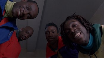 Movie still from “Cool Runnings” (1993), directed by Jon Turteltaub – A group of men standing next to each other in front of a wall; Medium shot, Low angle