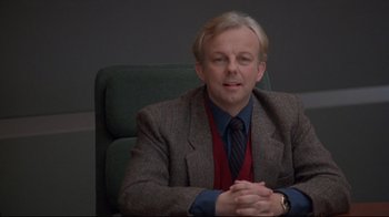 Movie still from “Cool Runnings” (1993), directed by Jon Turteltaub – A man sitting in a chair with his hands clasped together; Close Up shot, High angle