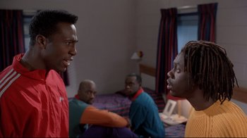 Movie still from “Cool Runnings” (1993), directed by Jon Turteltaub – A group of men sitting in a room talking to each other; Medium shot, Low angle