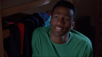 Movie still from “Cool Runnings” (1993), directed by Jon Turteltaub – A man sitting in a chair smiling for the camera; Close Up shot, High angle