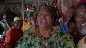 Movie still from “Cool Runnings” (1993), directed by Jon Turteltaub – An older woman wearing a green and yellow dress; Close Up shot, Low angle