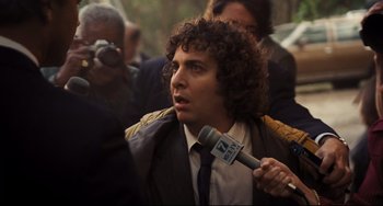 Movie still from “The Front Runner” (2018), directed by Jason Reitman – A man with curly hair is holding a microphone; Close Up shot, Over the shoulder angle