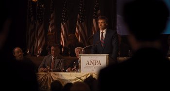 Movie still from “The Front Runner” (2018), directed by Jason Reitman – A man standing at a podium speaking at an anpa convention; Medium shot, High angle
