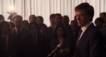 Movie still from “The Front Runner” (2018), directed by Jason Reitman – A man in a suit is speaking at a microphone; Close Up shot, Over the shoulder angle