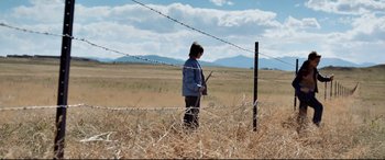 Movie still from “Cop Car” (2015), directed by Jon Watts – A woman standing in a field holding a stick; Wide shot, Low angle