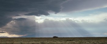 Movie still from “Cop Car” (2015), directed by Jon Watts – A car is parked in the middle of a field under a cloudy sky; Extreme Wide shot, Low angle