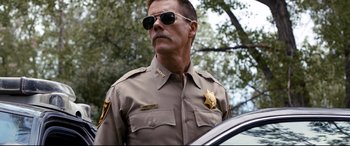 Movie still from “Cop Car” (2015), directed by Jon Watts – A man in a sheriff's uniform standing next to a police car; Close Up shot, Low angle