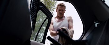 Movie still from “Cop Car” (2015), directed by Jon Watts – A man in a white tank top is looking at a car window; Medium shot, Low angle