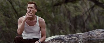 Movie still from “Cop Car” (2015), directed by Jon Watts – A man sitting on top of a rock smoking a cigarette; Medium shot, Low angle