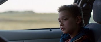 Movie still from “Cop Car” (2015), directed by Jon Watts – A boy sitting in the back seat of a car looking out the window; Close Up shot, Over the shoulder angle