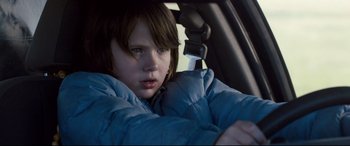 Movie still from “Cop Car” (2015), directed by Jon Watts – A young child sitting in the driver's seat of a car; Close Up shot, Over the shoulder angle