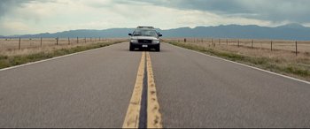 Movie still from “Cop Car” (2015), directed by Jon Watts – A car driving down the middle of the road; Extreme Wide shot, Low angle