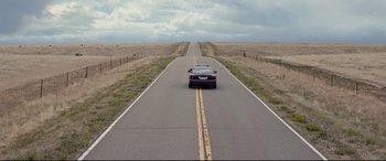 Movie still from “Cop Car” (2015), directed by Jon Watts – A car driving down the middle of a road; Extreme Wide shot, High angle