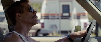 Movie still from “Cop Car” (2015), directed by Jon Watts – A person wearing sunglasses driving a car; Close Up shot, Over the shoulder angle