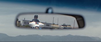 Movie still from “Cop Car” (2015), directed by Jon Watts – A man in a police uniform is seen in a side mirror; Wide shot, Low angle