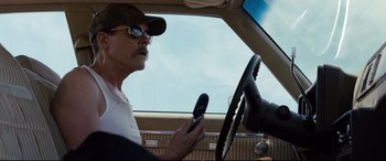 Movie still from “Cop Car” (2015), directed by Jon Watts – A man in a car holding a cell phone to his ear; Close Up shot, Low angle